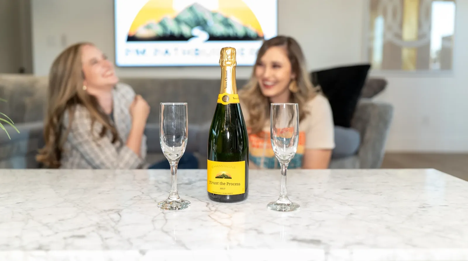 A bottle labelled Trust the Process on a marble counter, with The PathBuilders team celebrating behind it.